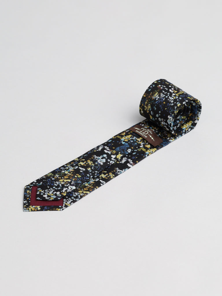 The Liberty of London Tana Lawn™ Reflection Tie by ID Menswear features a blue, yellow, and white floral pattern on premium cotton, a maroon tip, visible brand label inside, and is styled rolled-up against a dark background.