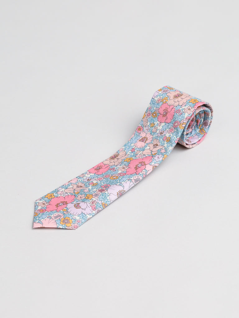 The Liberty of London Tana Lawn™ Pink Lawn Tie by ID Menswear features a vibrant floral pattern in pink, blue, orange, and white, handcrafted in Brooklyn from premium Tana Lawn cotton. Shown partially rolled on a light gray background.