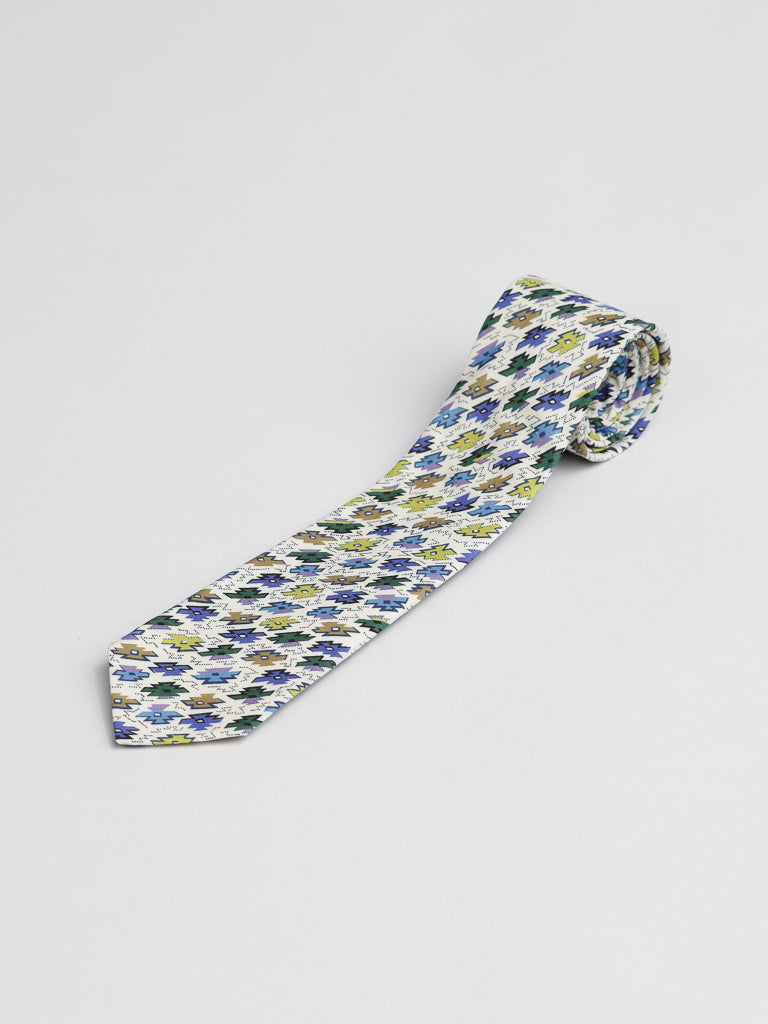 A rolled-up Liberty of London Tana Lawn™ Sunrise Tie by ID Menswear, handmade in Brooklyn with blue, green, and yellow floral patterns on white cotton, displayed on a plain white surface.