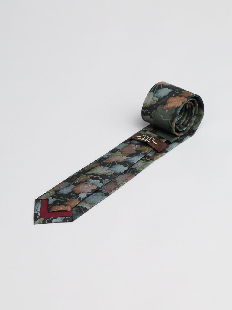 The Liberty of London Tana Lawn™ Cloud Nine Tie by ID Menswear, handmade in Brooklyn from soft cotton, features a camouflage leaf pattern in brown, green, and gray. It is dark green, rolled at one end, and set on a white background.