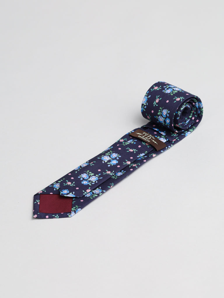 The Liberty of London Tana Lawn™ Magdalena Tie by ID Menswear, handmade in Brooklyn from fine cotton and featuring a blue and white floral pattern, is rolled at one end and displayed on a light gray background.