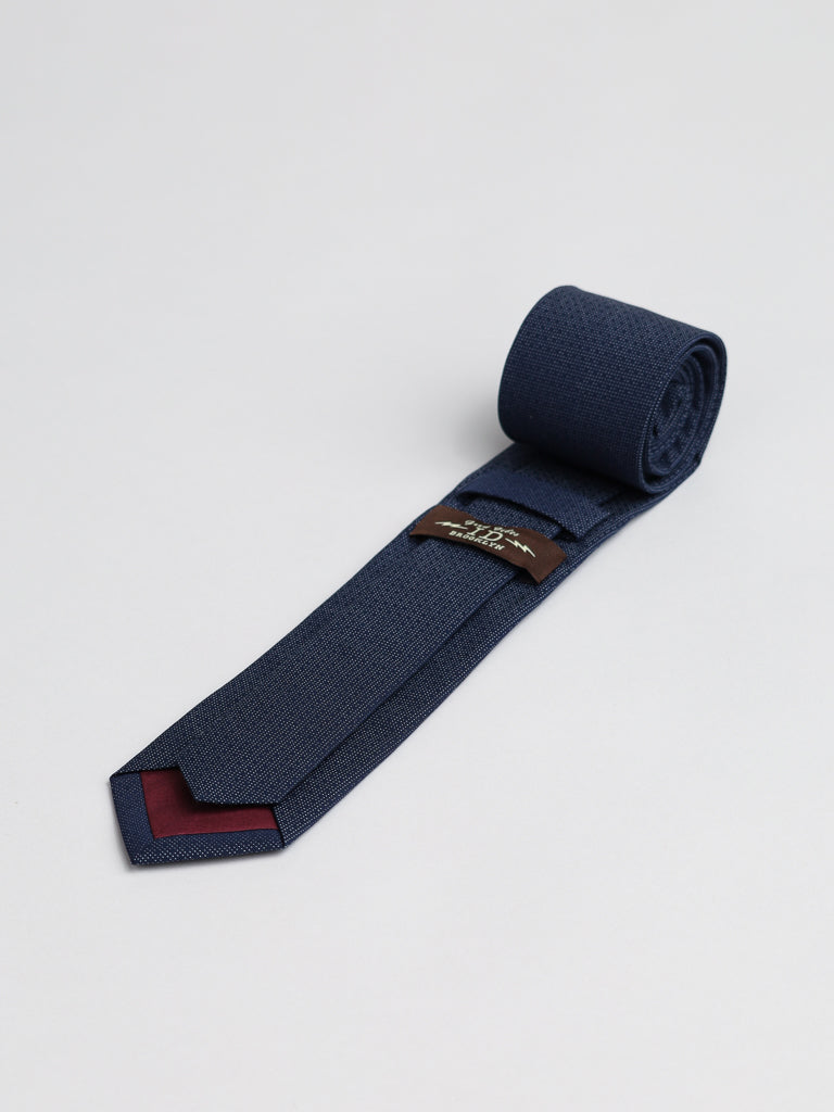 The Starry Night Cotton Tie by ID Menswear is a rolled-up navy blue textured formal tie featuring a maroon accent on the pointed end and a visible brown label along the back, displayed on a light gray surface.