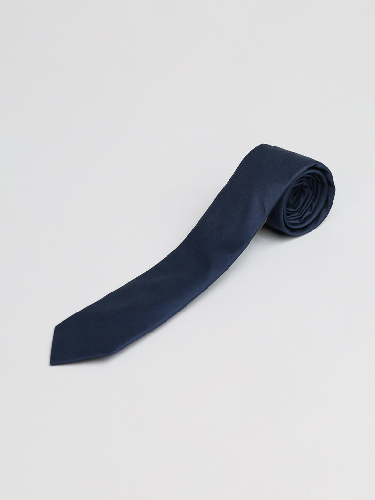 The Midnight Cotton Tie by ID Menswear, a navy blue cotton accessory handmade in Brooklyn, is shown neatly rolled on a plain, light surface.