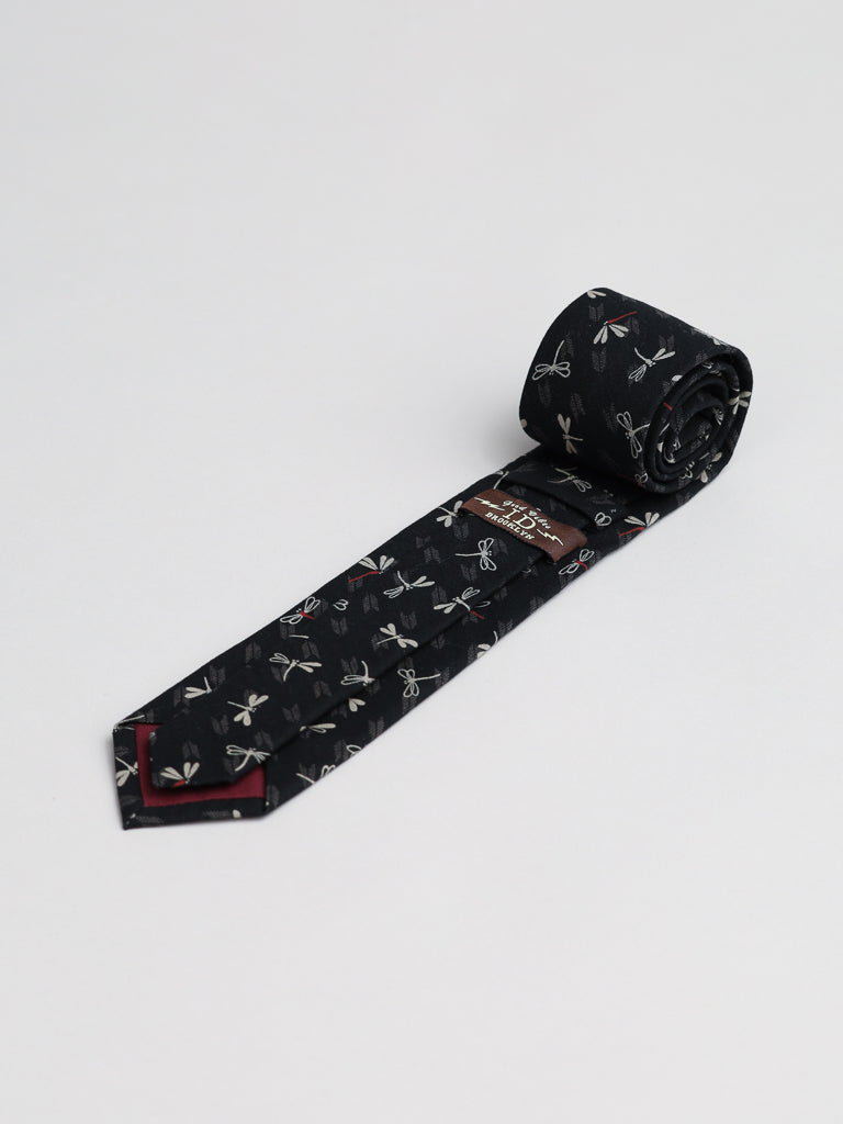 The Japanese Printed Dragonfly Tie by ID Menswear, featuring a repeating small dragonfly motif in black, is handmade in Brooklyn and shown neatly rolled on a plain white background.
