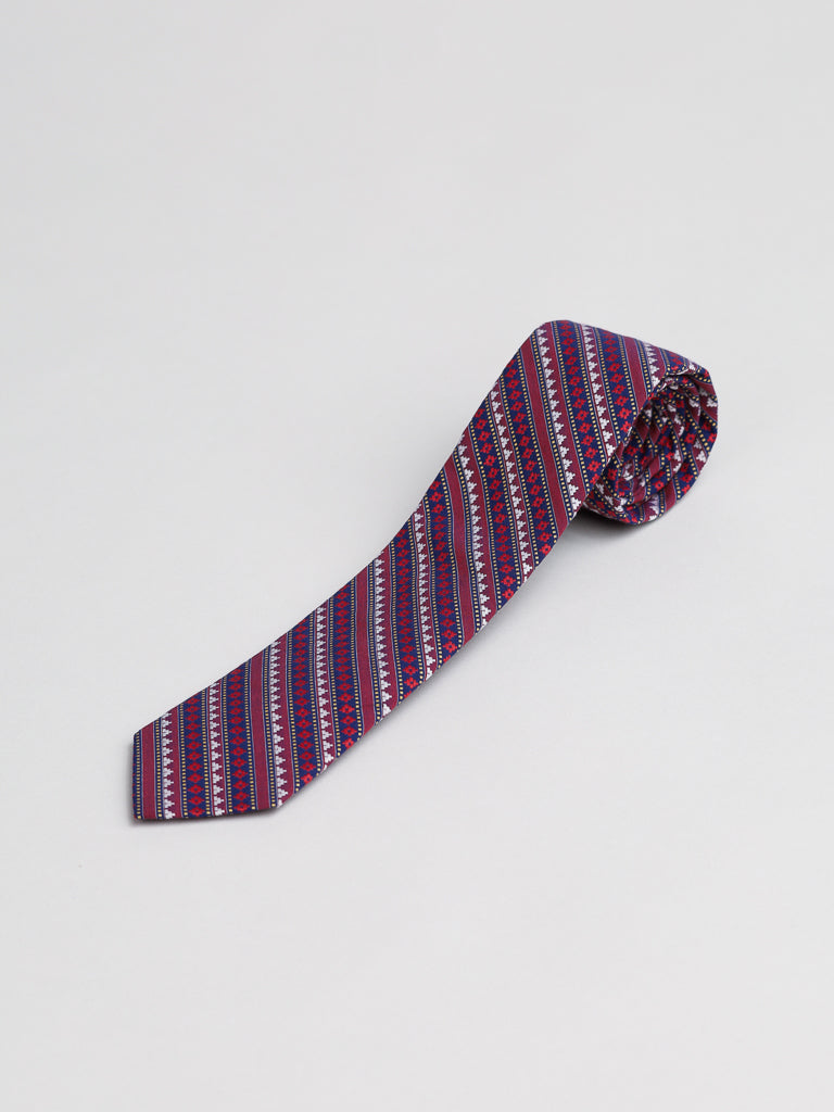 The Karuna Cotton Tie by ID Menswear, handmade in Brooklyn, features diagonal stripes in purple, blue, and white—ideal for business formal attire. Displayed rolled up on a plain light background.