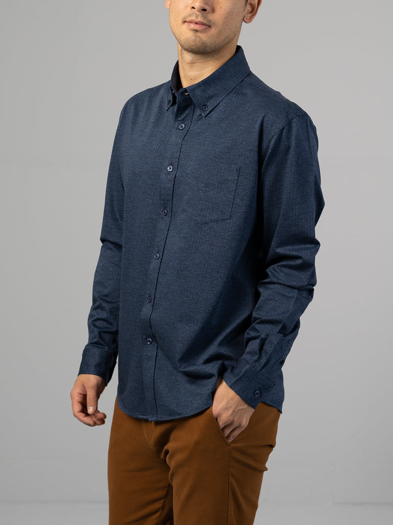 A person wearing a dark blue Leo Stretch Button Down Shirt by ID Menswear with brown pants stands against a gray background. One hand is in the pants pocket, and their relaxed posture exudes confidence, highlighting the shirts high-quality finish.
