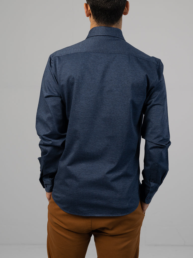 A man, facing away, is wearing an ID Menswear Leo Stretch Button Down Shirt in dark blue and brown pants. The high-quality finish enhances the sleek look against a plain, light-colored background.