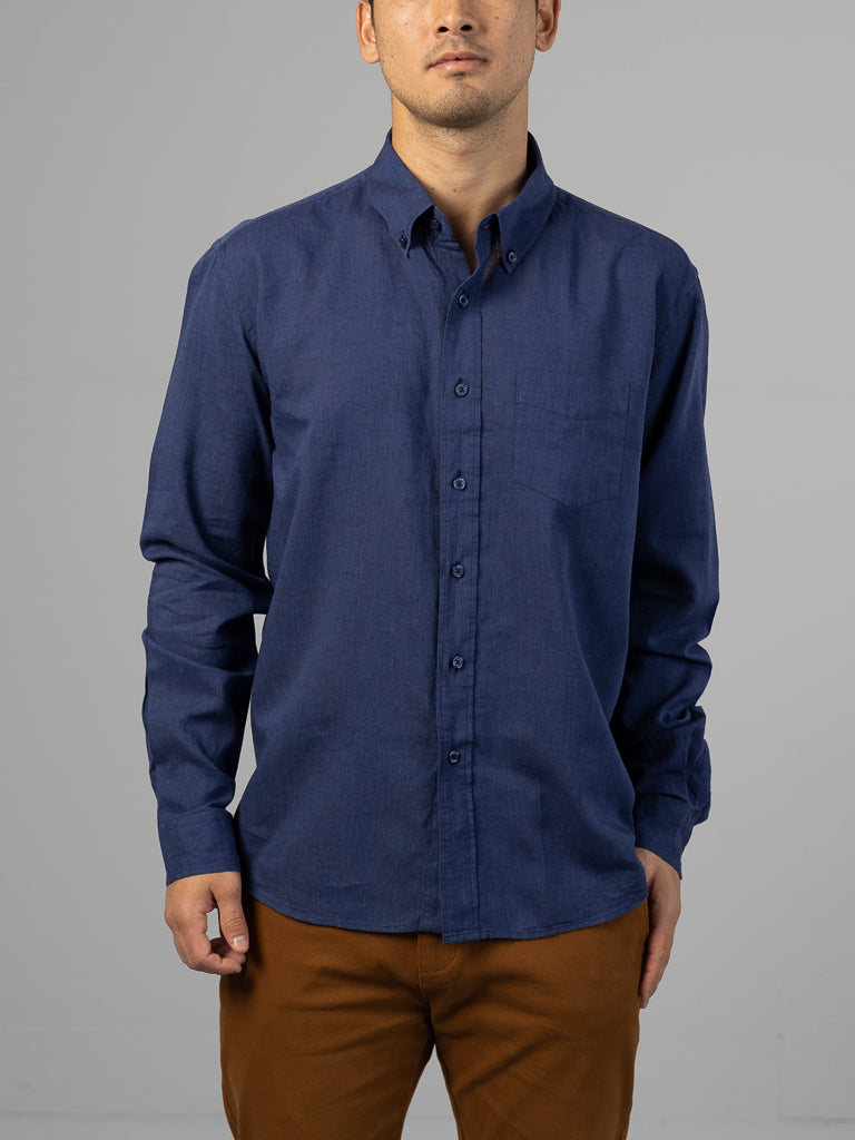 A man in a Marcus Linen Blend Button Down Shirt by ID Menswear and brown pants stands against a plain backdrop. His head tilts slightly left, with one hand casually in his pocket.