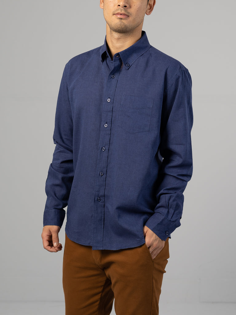 A man stands with one hand in his pocket, wearing an ID Menswear Marcus Linen Blend Button Down Shirt in dark blue and brown pants against a plain gray background.