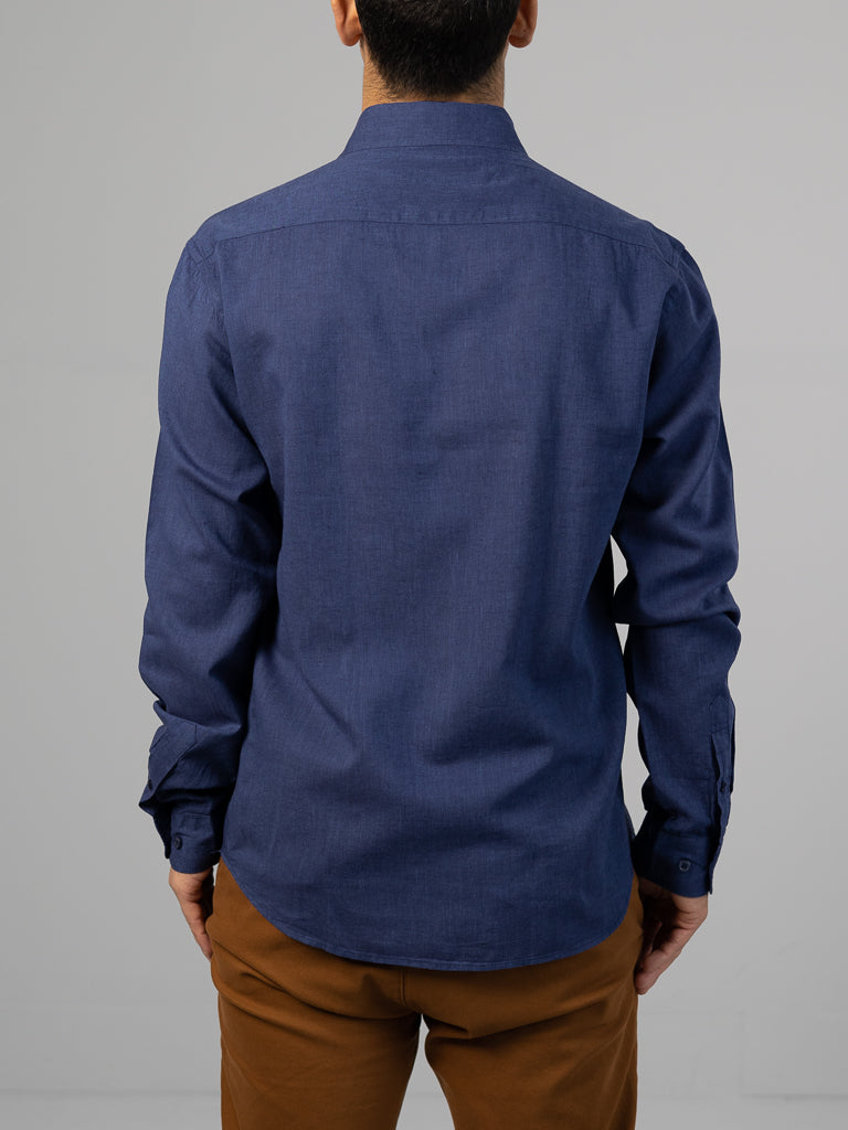 A person with short dark hair is seen from behind, wearing the Marcus Linen Blend Button Down Shirt by ID Menswear. The dark blue regular-fit shirt features a button-down collar and long sleeves and is paired with brown pants against a plain light gray background.