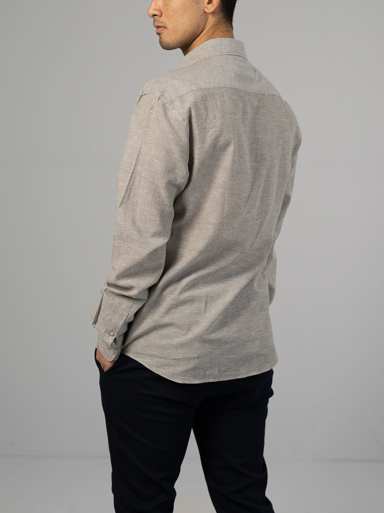 A person in an ID Menswear Marcus Linen Blend Button Down Shirt, colored light gray and regular-fit, paired with black pants, stands with their back to the camera against a plain light gray background.