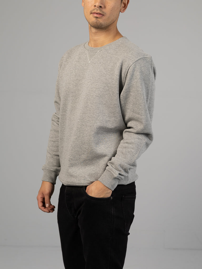 Against a plain gray background, an individual wears the ID Menswear Everyday French Cotton Terry Crewneck Sweatshirt in gray. With one hand in their pocket, they gaze slightly to the left under soft, even lighting.