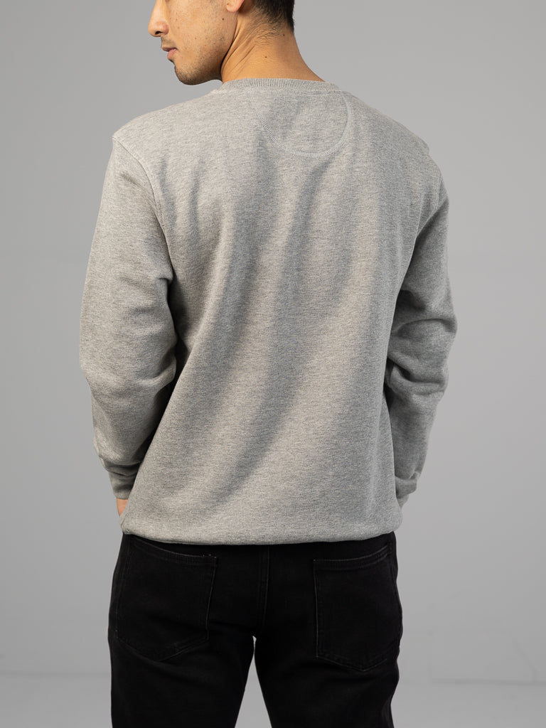 A person wearing an ID Menswear Everyday French Cotton Terry Crewneck Sweatshirt in gray and black pants stands with their back to the camera against a plain gray background, hands tucked into pockets.