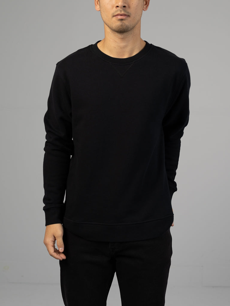 Against a neutral backdrop, a person wears an Everyday French Cotton Terry Crewneck Sweatshirt in black by ID Menswear. Their face is obscured, and their outfit includes matching black pants.
