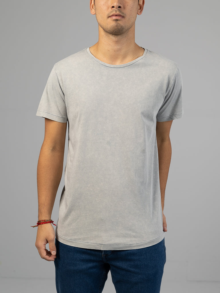 Against a plain gray backdrop, an individual with short hair wears the Legacy Organic Cotton Tee by ID Menswear in light gray and dark blue jeans. A red string bracelet adorns their right wrist, exuding a classic, vintage look focused on their upper body.