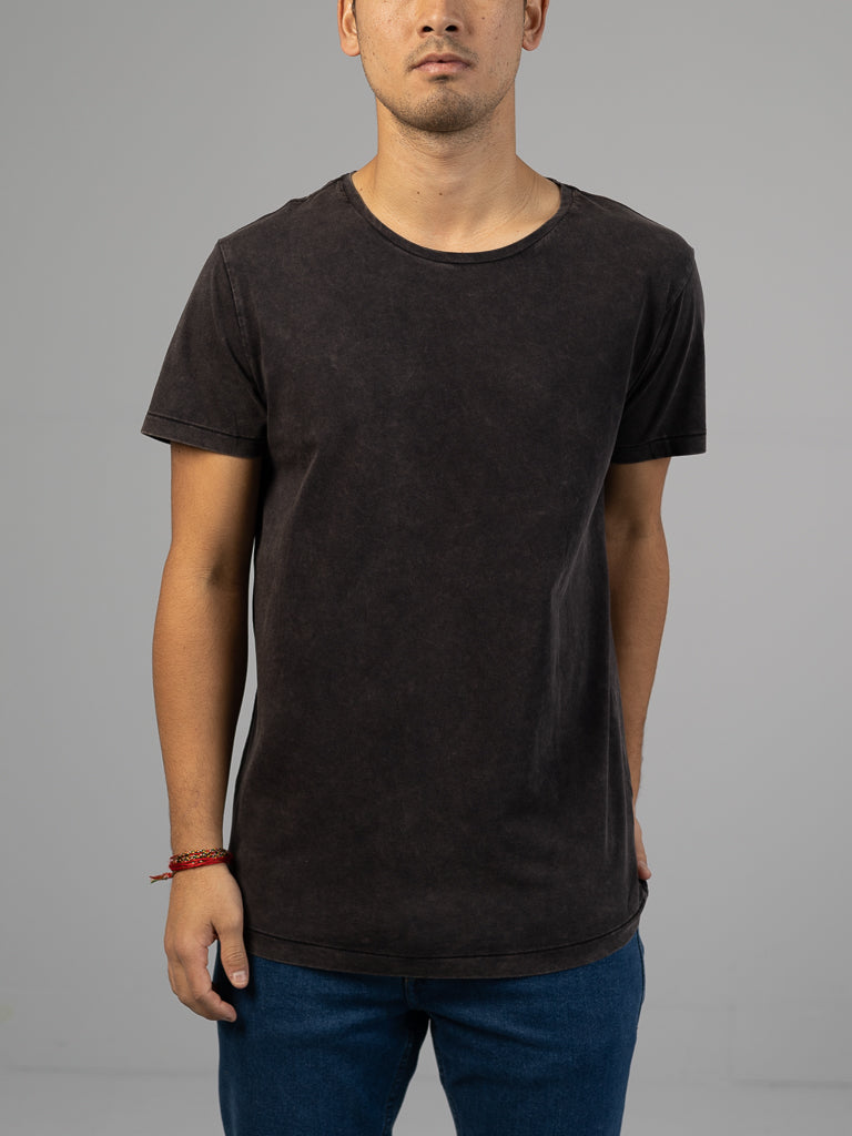 Wearing ID Menswears Legacy Organic Cotton Tee in classic fit, plain black with blue jeans and a red bracelet on the left wrist, the person stands against a neutral gray background. The head is partially out of frame, emphasizing the comfortable organic cotton attire.