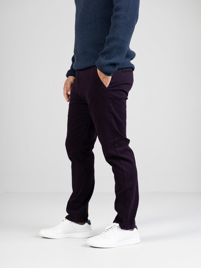 A person stands against a plain backdrop wearing an ID Menswear blue sweater, regular slim-fit Banker Twill Stretch Chino, and white sneakers. Their hands are in their pockets, highlighting a casual style.