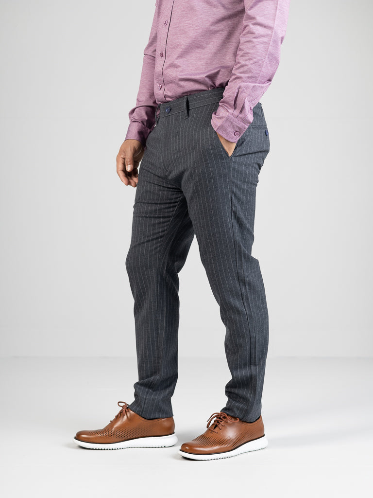 A person wears a purple shirt with Hudson Wool Blend Pin Stripe Pants by ID Menswear, featuring gray pinstriped mid-rise slim-fit design, hands in pockets. They pair them with brown shoes and white soles against a plain light background.