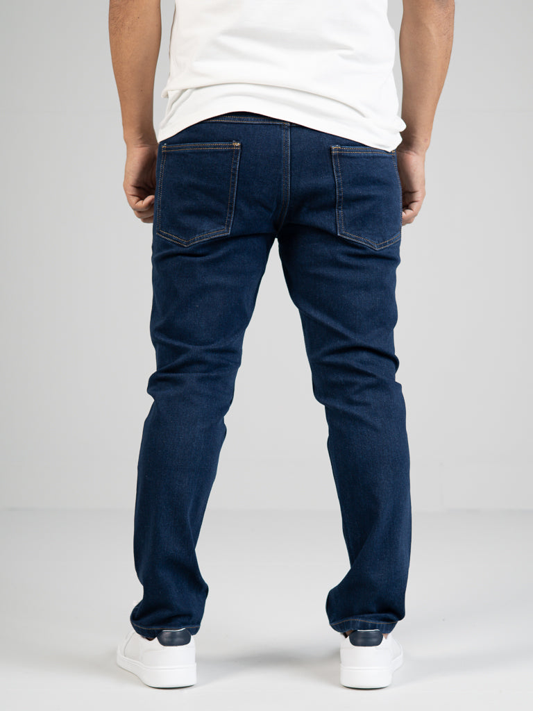 A person in ID Menswears Ganbaru Stretch Jean and a white shirt stands against a plain background, paired with white sneakers featuring dark soles.