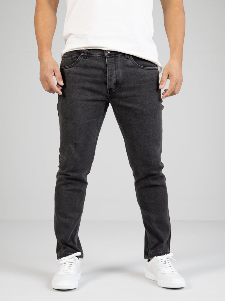 Someone wearing ID Menswears Ganbaru Stretch Jean, which features a slim-tapered fit, stands against a light gray background. The white T-shirt and sneakers complement the stylish silhouette of the jeans.