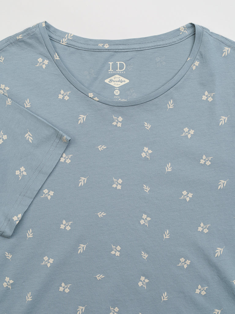 The Heritage Printed Organic Cotton Tee by ID Menswear is a blue T-shirt with a round neckline and short sleeves, featuring a hand screen printed pattern of small white floral designs.