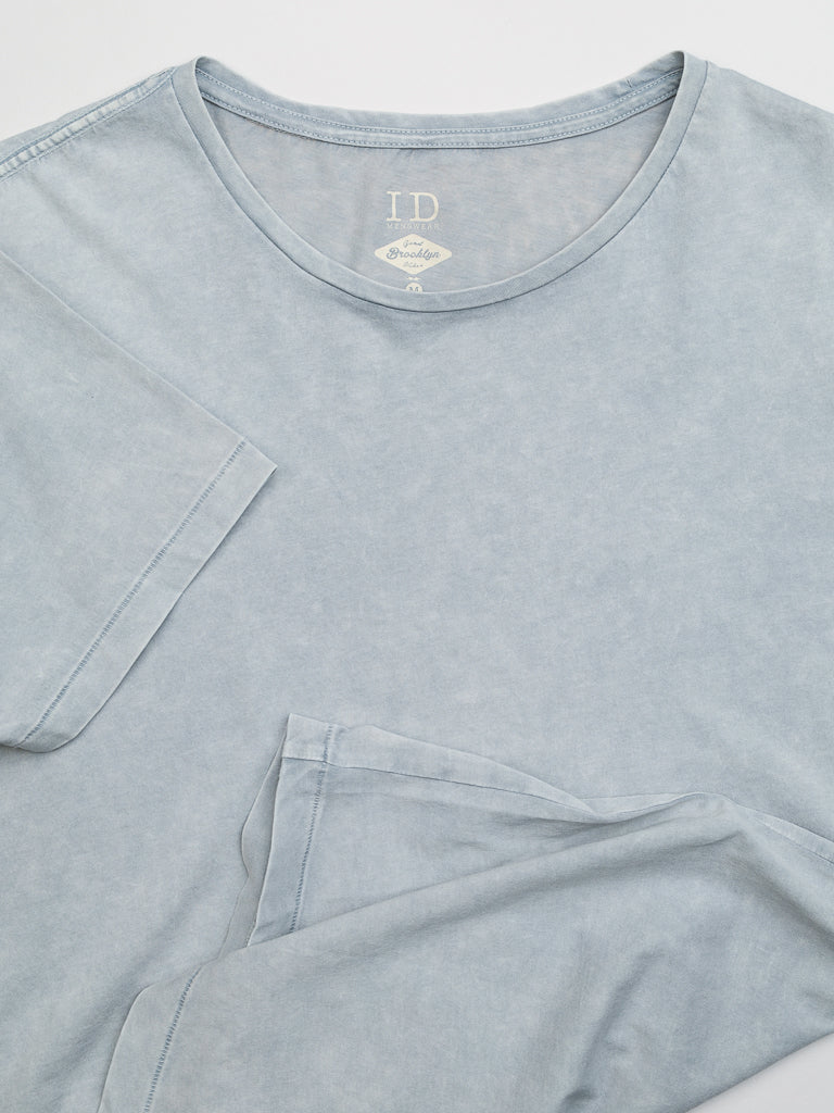 The Legacy Organic Cotton Tee by ID Menswear is a vintage-look, light blue, short-sleeve crew neck made from organic cotton. It has a soft, slightly faded fabric with an inner collar tag showing ID and care instructions. Neatly displayed for presentation.