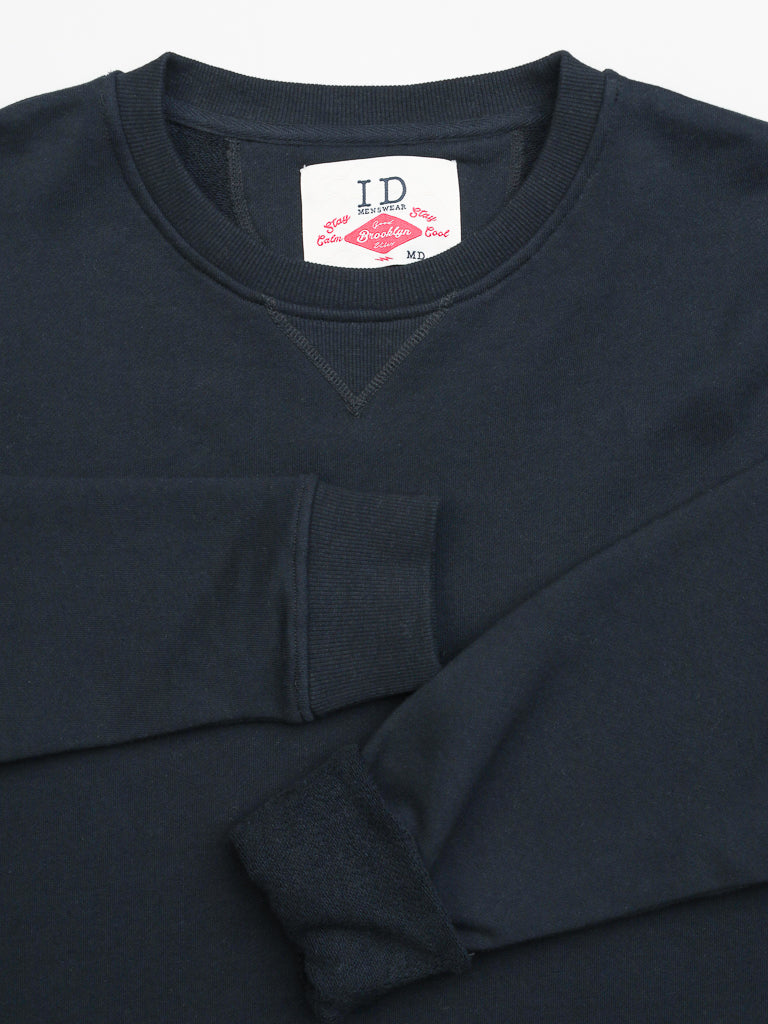 A navy blue Everyday French Cotton Terry Crewneck Sweatshirt from ID Menswear is neatly folded, featuring a round neckline and long sleeves. Inside the collar, a label provides care instructions and additional details.