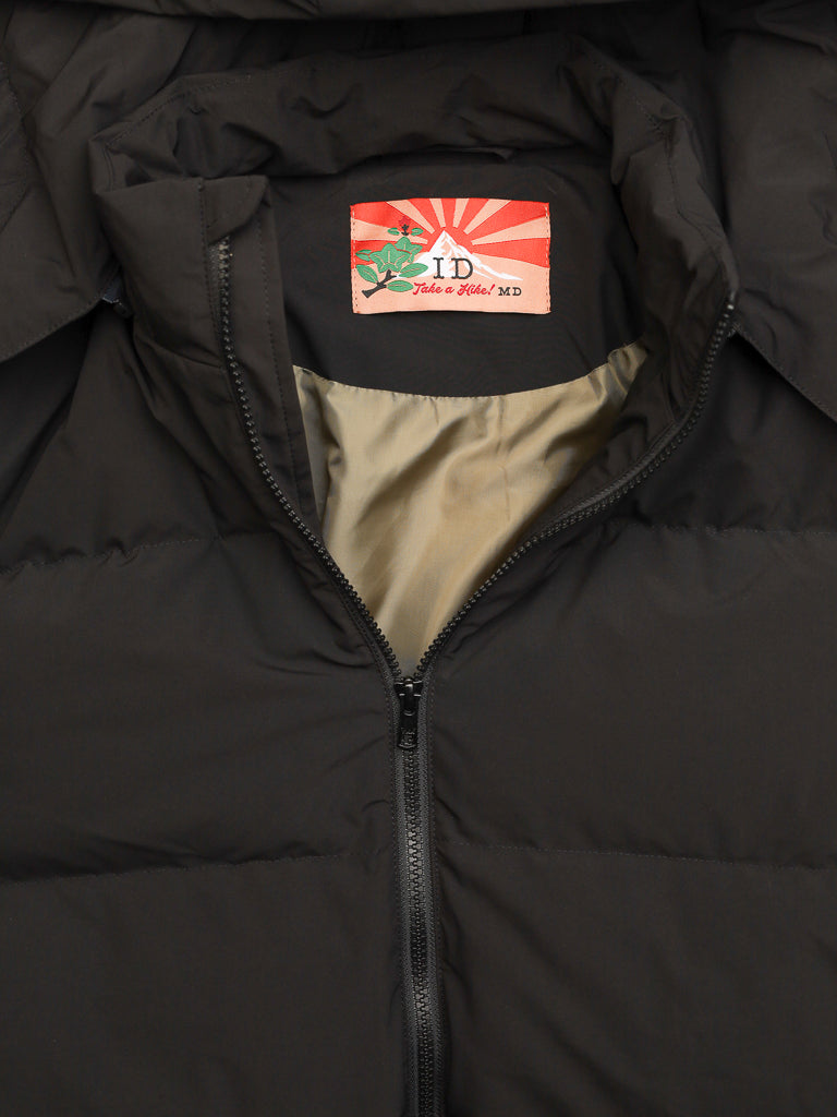 A close-up of the Arctic Black Puffer Down Jacket by ID Menswear, partially unzipped to reveal its beige lining and a collar label featuring "ID" with a red sunburst and green vine design.