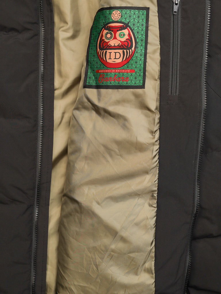 Close-up of the inner lining of the Arctic Black Puffer Down Jacket by ID Menswear, showing a green and red patch with a daruma doll design, the letters ID, and "Crickets" stitched in red below.