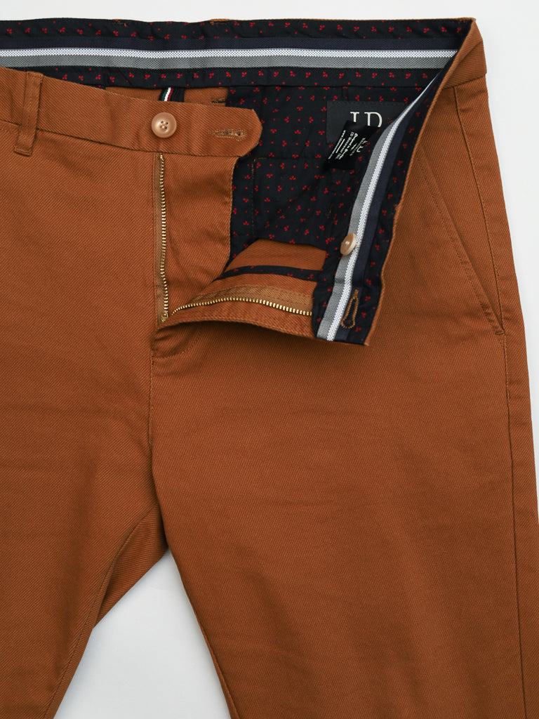 The Wythe Twill Stretch Chino by ID Menswear are slim-fit cotton twill pants in brown, showcasing a partially open zipper and button with a dark lining featuring a small red pattern. Inside, they have a white ID label, and the waistbands striped detail adds to their casual charm.