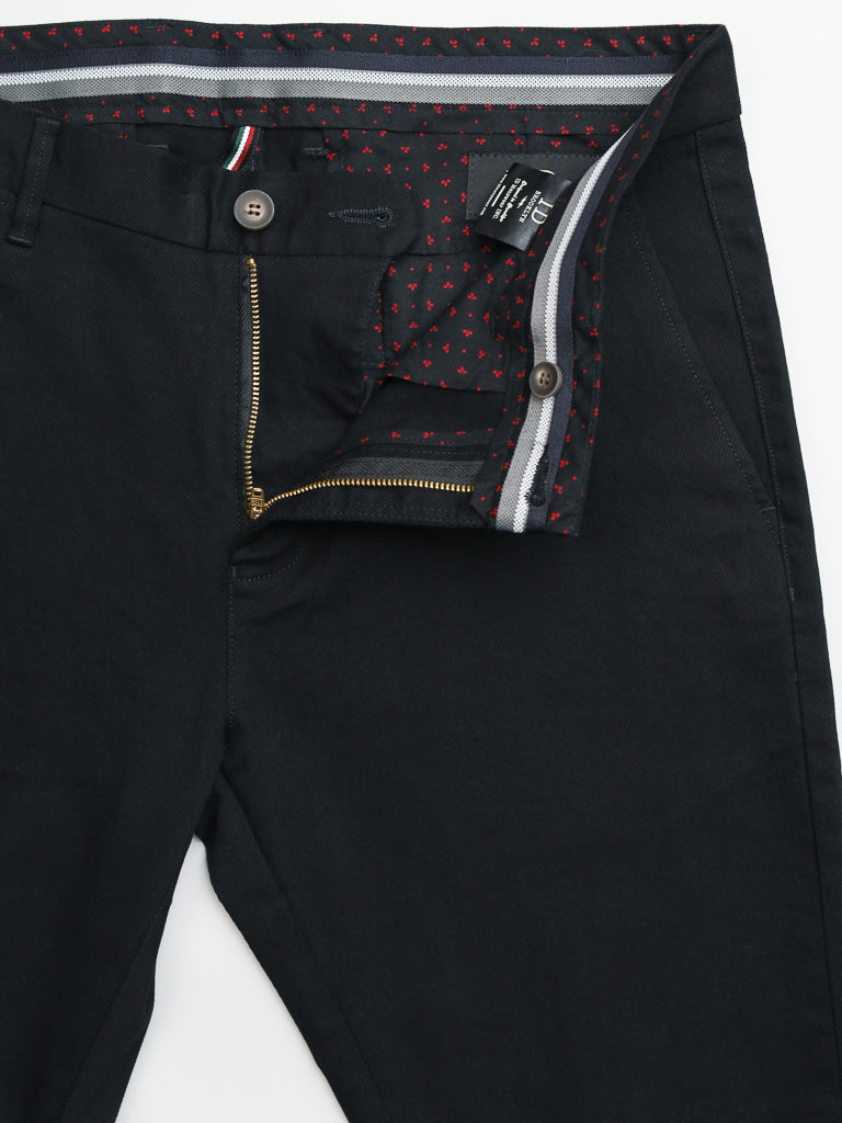 The Wythe Twill Stretch Chino by ID Menswear is a slim-fit pant with a zipper and button revealing a red heart patterned lining. Made from cotton twill, it has a white and gray striped waistband, ideal for casual wear. A clothing tag is visible inside.