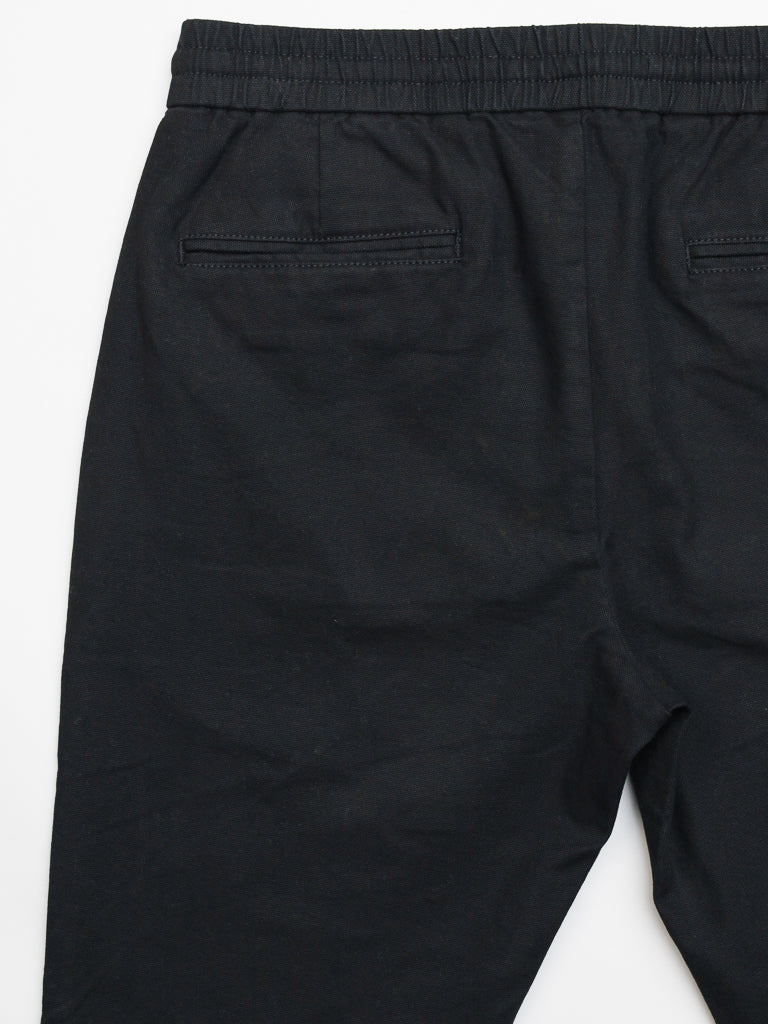 The Kent Drawstring Canvas Pant by ID Menswear is a slim-fit, mid-rise black pant with an elastic waistband and two back welt pockets. Made from smooth, slightly wrinkled cotton canvas, they are displayed on a white background.