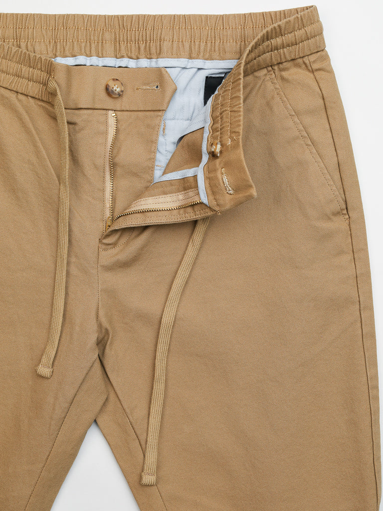 Close-up of ID Menswears Kent Drawstring Canvas Pant: tan slim-fit mid-rise with elastic waistband, drawstring, and open zipper fly revealing a light blue inner lining. These cotton canvas pants offer casual comfort and style for everyday wear.