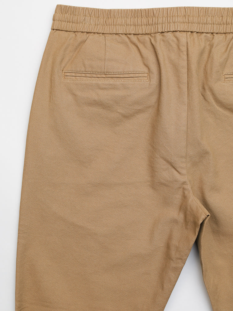 A close-up of the Kent Drawstring Canvas Pant by ID Menswear shows beige, slim-fit mid-rise pants featuring an elastic waistband made of smooth, slightly wrinkled cotton canvas with two neat rear welt pockets.