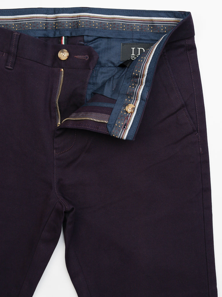 The Banker Twill Stretch Chino by ID Menswear features a dark purple hue with a partially open zipper, a blue patterned waistband lining, and visible button closure. The interior label reads HD. These regular slim-fit mid-rise pants are shown flat on a white background.