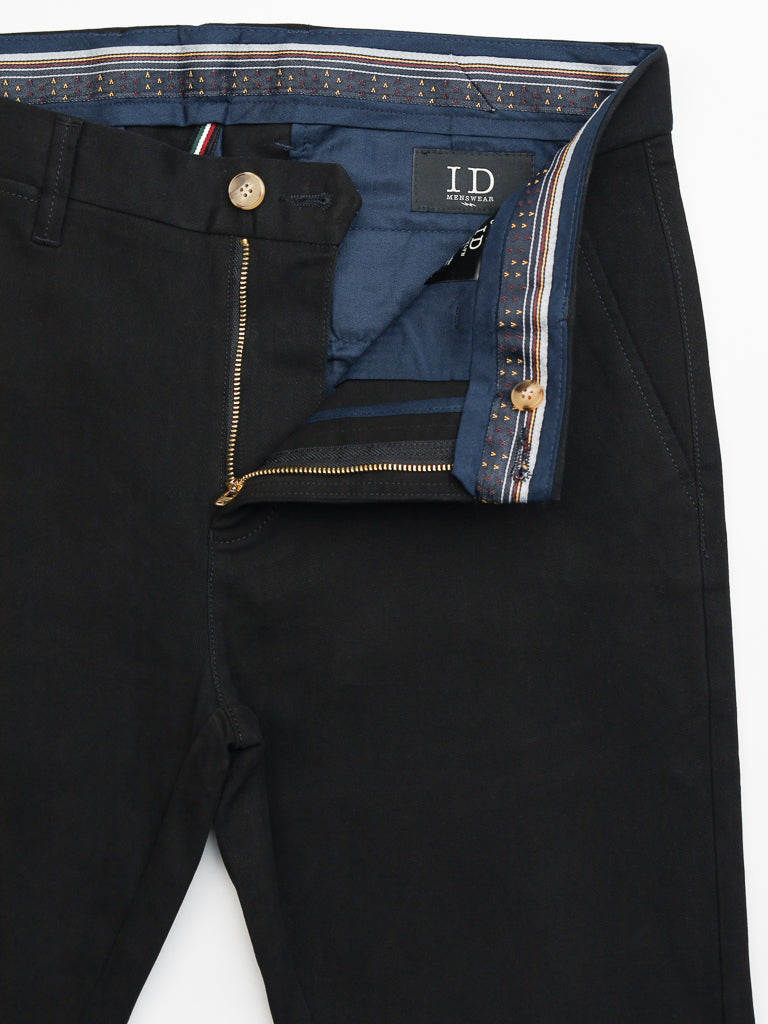 Black ID Menswear Banker Twill Stretch Chinos, regular slim fit and mid-rise, feature a partially open fly revealing a blue striped inner lining. They include a visible button above the fly, and the waistband edge exhibits a multicolored striped design.