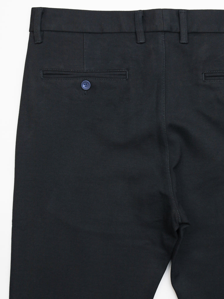 The Manhattan 4-way Stretch Dress Pant by ID Menswear is shown from the back, highlighting a blue button on one rear pocket. These black slim-fit pants feature wrinkle-resistant fabric, belt loops at the waistband, and offer a smooth, well-tailored business casual look.