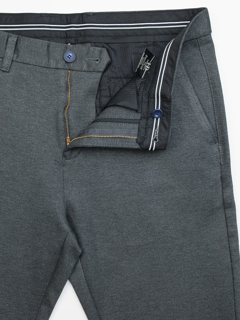The Manhattan 4-way Stretch Dress Pant by ID Menswear is wrinkle-resistant and dark gray, featuring a striped waistband visible through a partially open zipper, front pockets, and a blue button at the waistband. This slim-fit design is ideal for business casual and everyday wear.