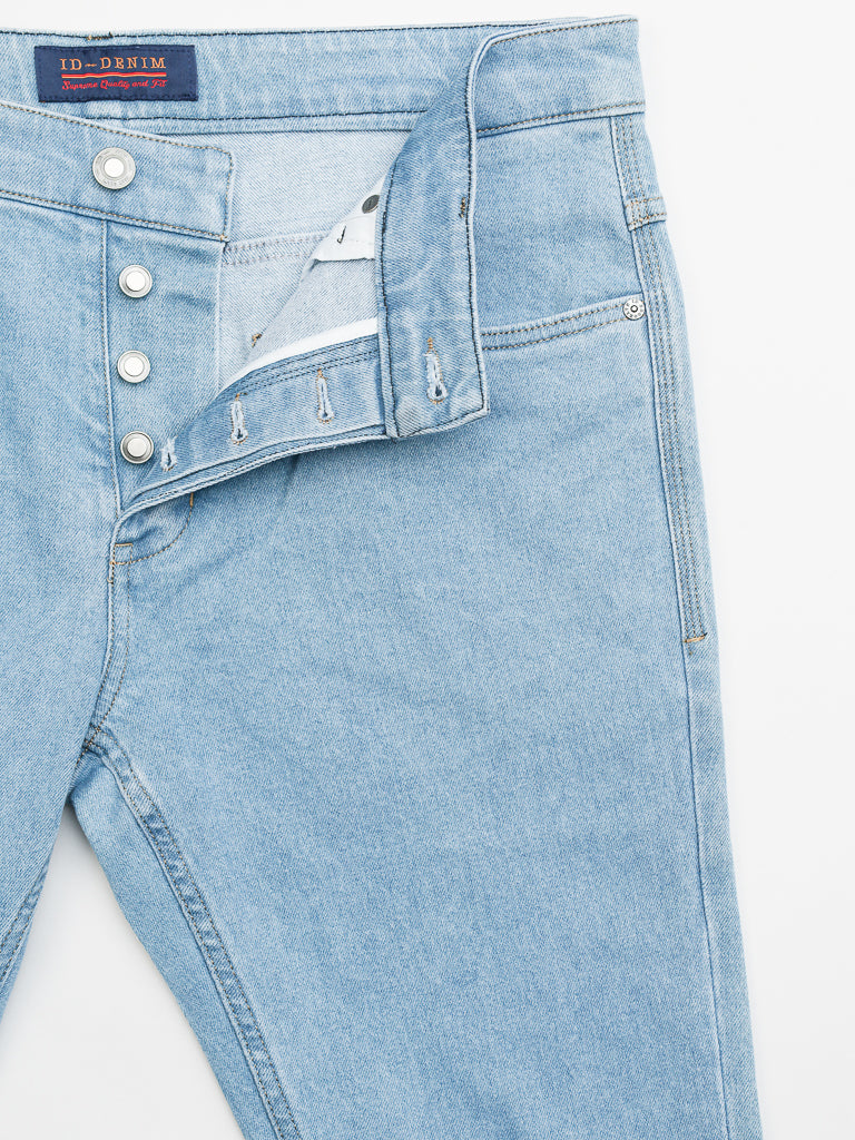 The Ganbaru Stretch Jean by ID Menswear features a slim-tapered fit with a button-fly closure in light blue denim. The cotton twill fabric is slightly faded, showcasing visible stitching on the pockets and seams, with the fly buttons and waist label partially open.