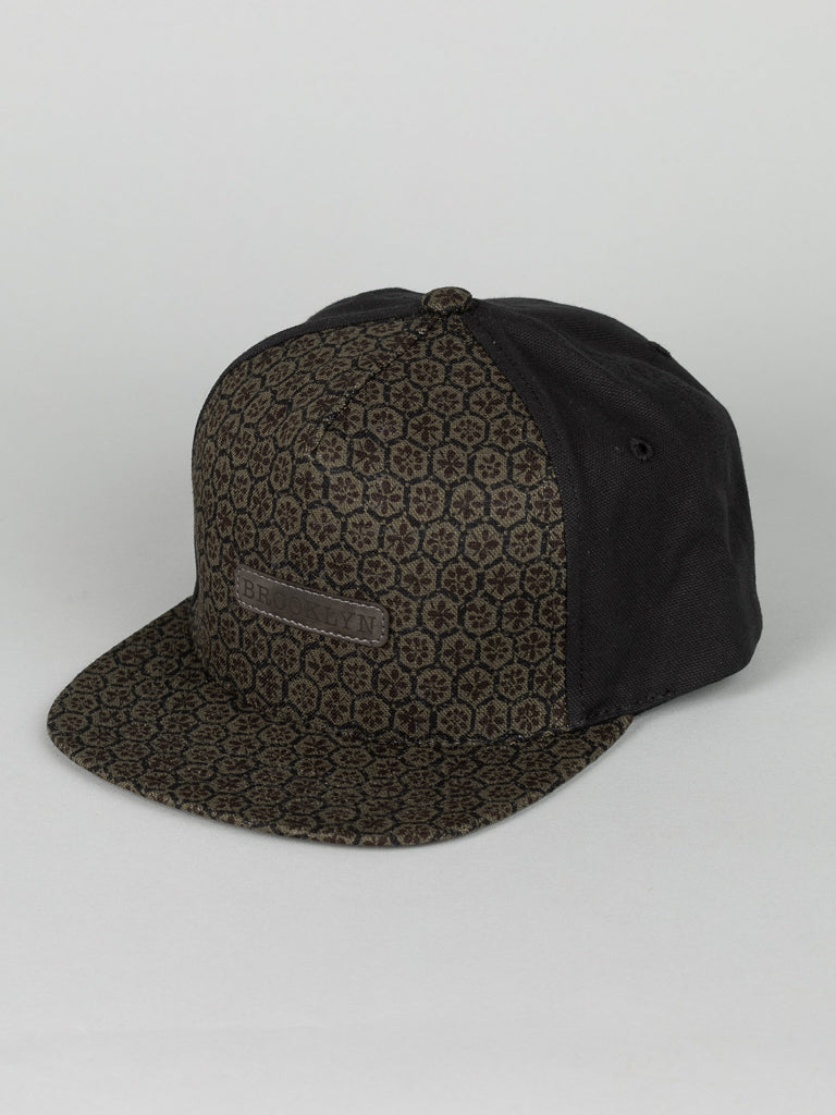 The ID Menswear Japanese Printed Osaka Cotton Trucker is a stylish black baseball cap made from 100% cotton, featuring a flat brim and an intricate hexagonal pattern on the front and brim.