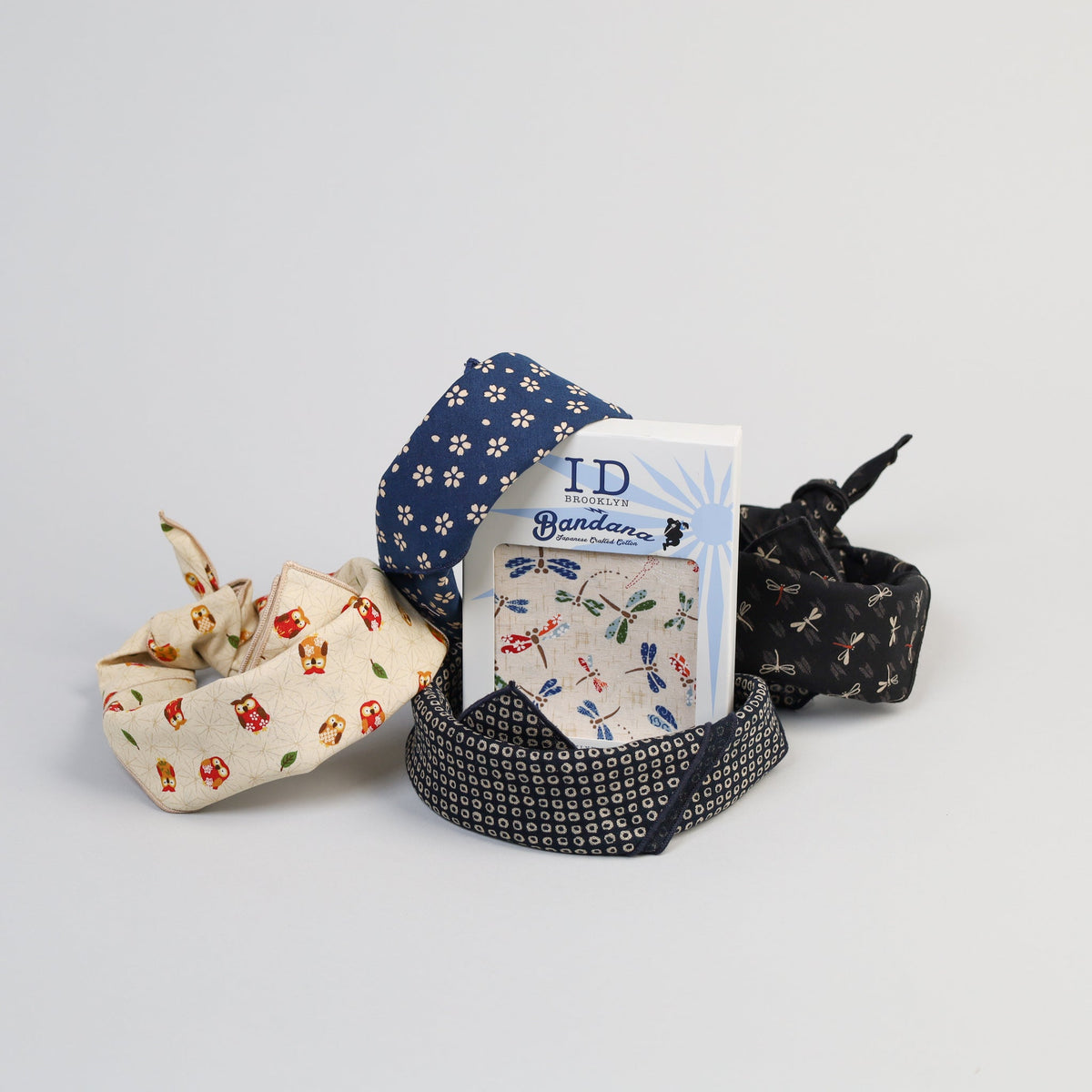 ID Menswears Japanese Wave Bandana collection includes four 100% cotton bandanas: one blue with white flowers, one cream with mushroom prints, one white featuring multicolored patterns, and a black bandana adorned with small geometric designs and a subtle Japanese wave pattern.
