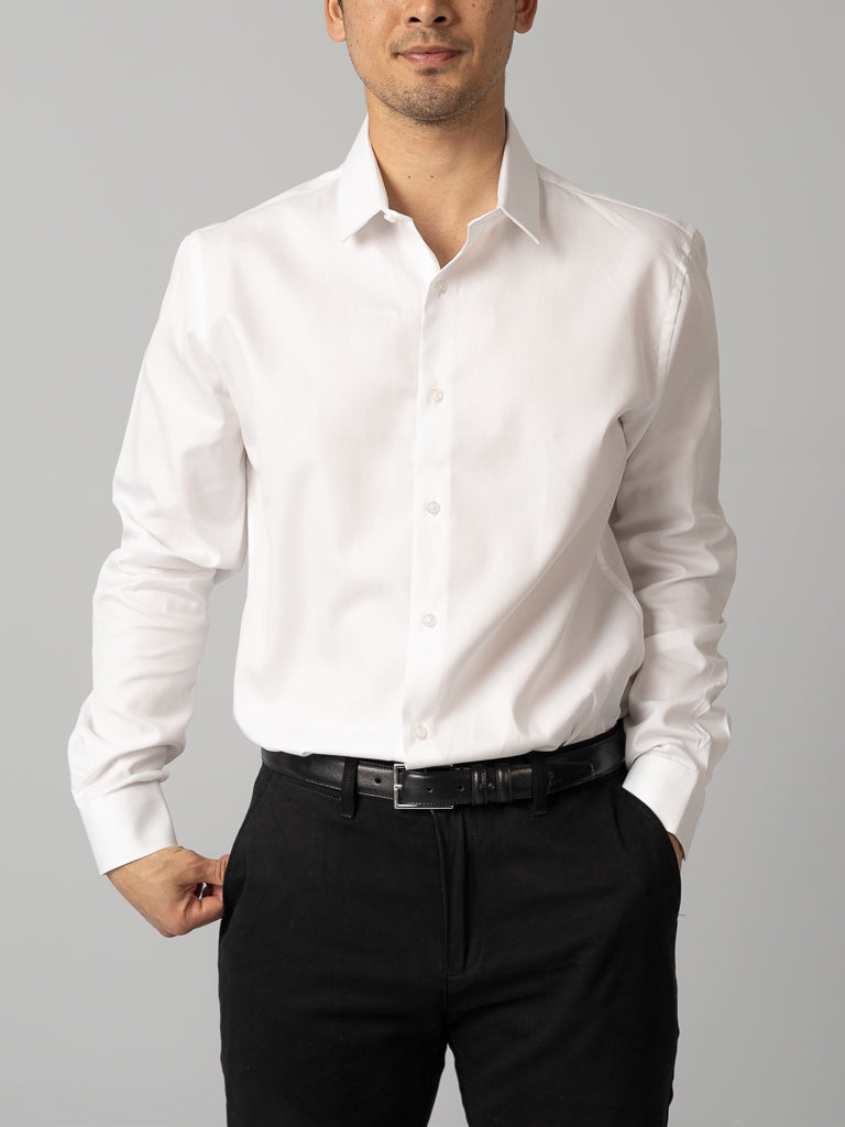 A man wears an ID Menswear Cotton Dress Shirt in slim fit paired with black pants, standing against a gray background with one hand in his pocket. His face is partially visible.
